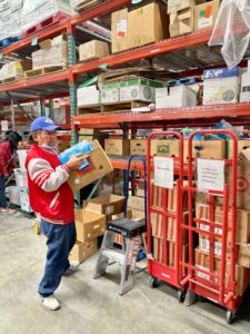 A man picks up a box of groceries in a store stockroom.