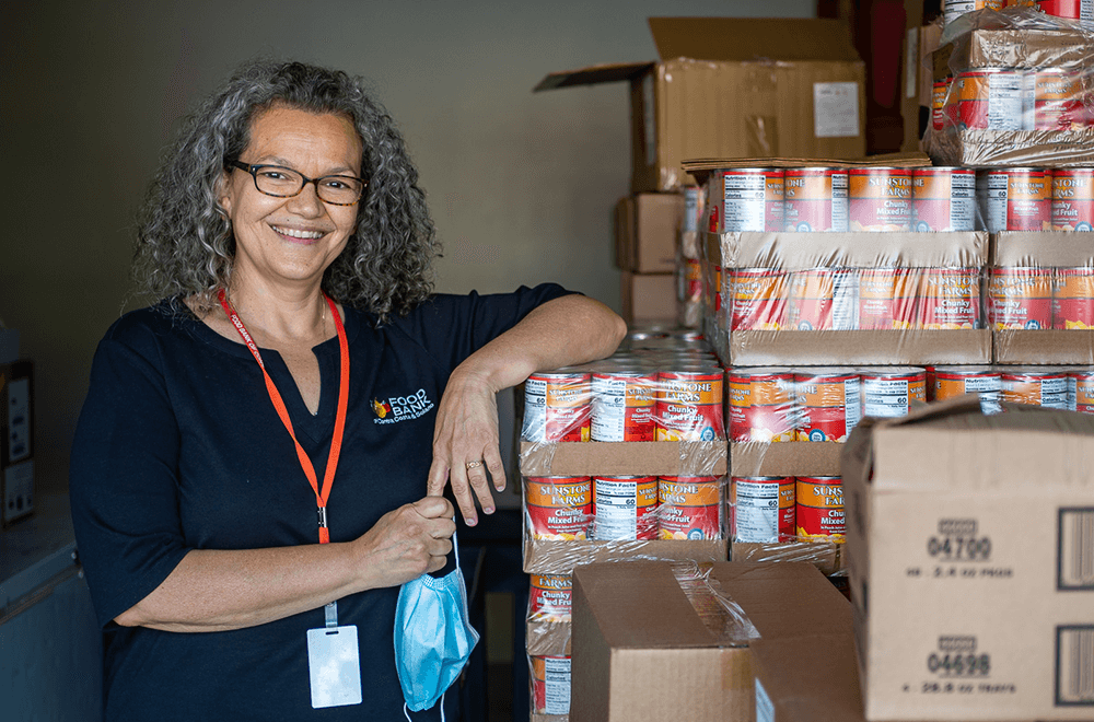 Un empleado del banco de alimentos posa junto a palets de alimentos enlatados almacenados.