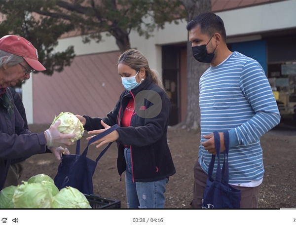 Volunteer hands cabbage to man and woman receiving food.