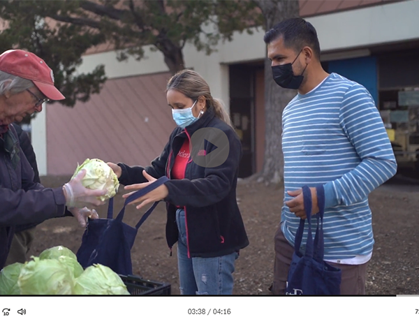 Un voluntario entrega repollo a un hombre y una mujer que reciben comida.