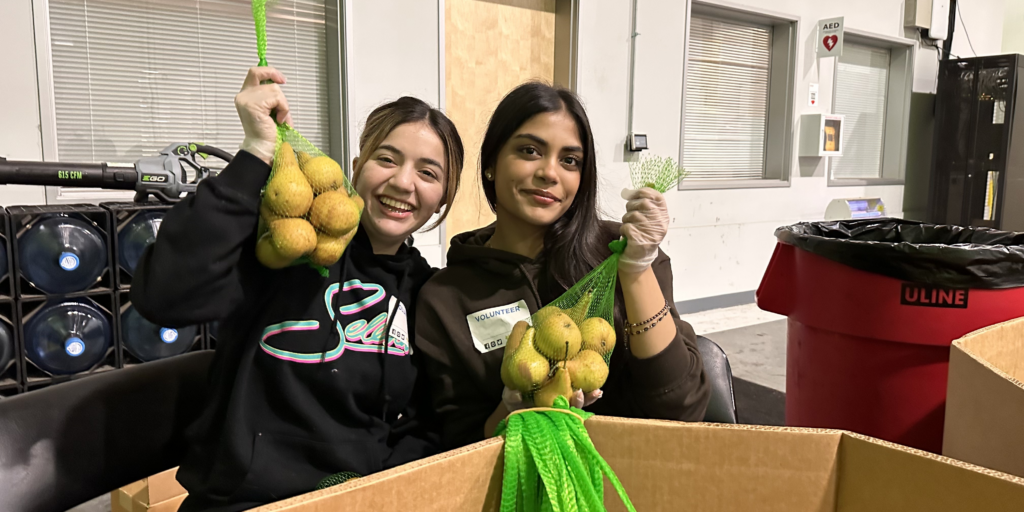 Two Food Bank volunteers holding bags of pears.