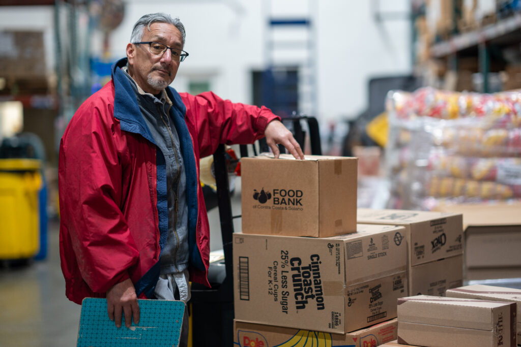 A man poses with boxes of food in the Food Bank warehouse.