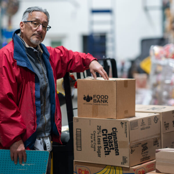 Un hombre posa con cajas de comida en el almacén del Banco de Alimentos.