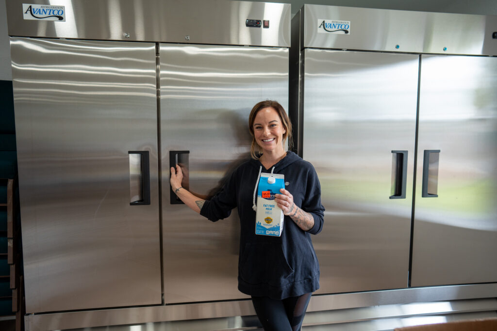 A volunteer poses with a carton of milk in front of a new commercial refrigerator. 