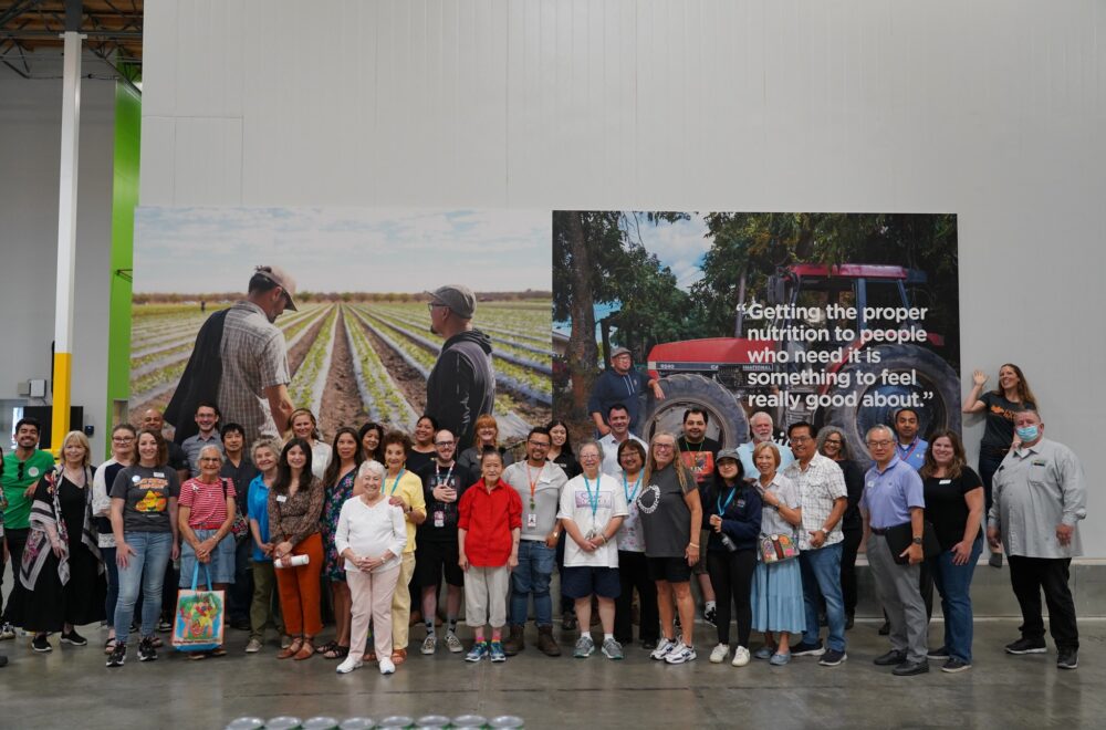 A large group of visitors pose in front of new artwork of our farm partners in our volunteer center.