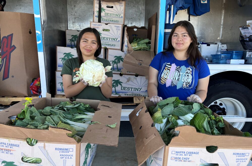Two young women hand out produce at a Food Bank distribution.