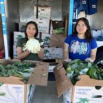 Two young women hand out produce at a Food Bank distribution.