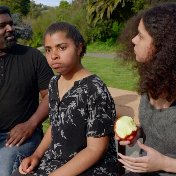 A father and his two teenage daughters eat apples in the park.