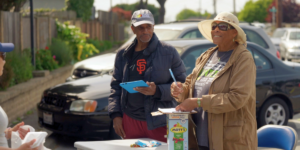 Dos voluntarios del banco de alimentos reciben a los vecinos en un punto de distribución.