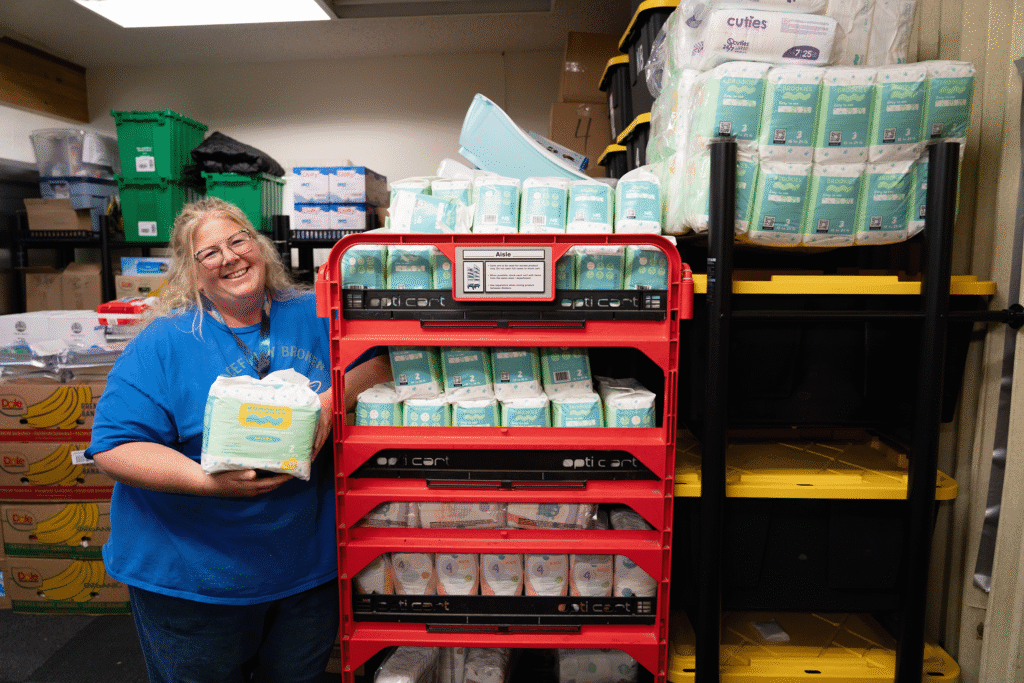 A blonde woman stands next to a rack of diapers.