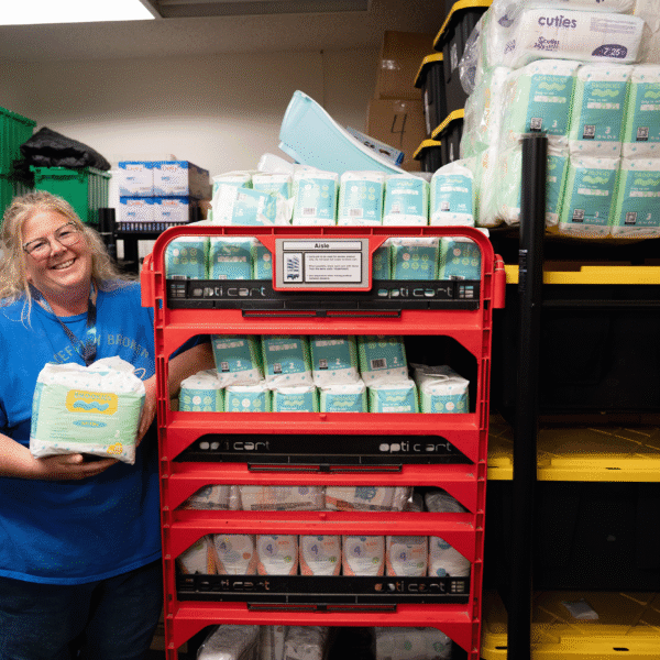 A blonde woman stands next to a rack of diapers.